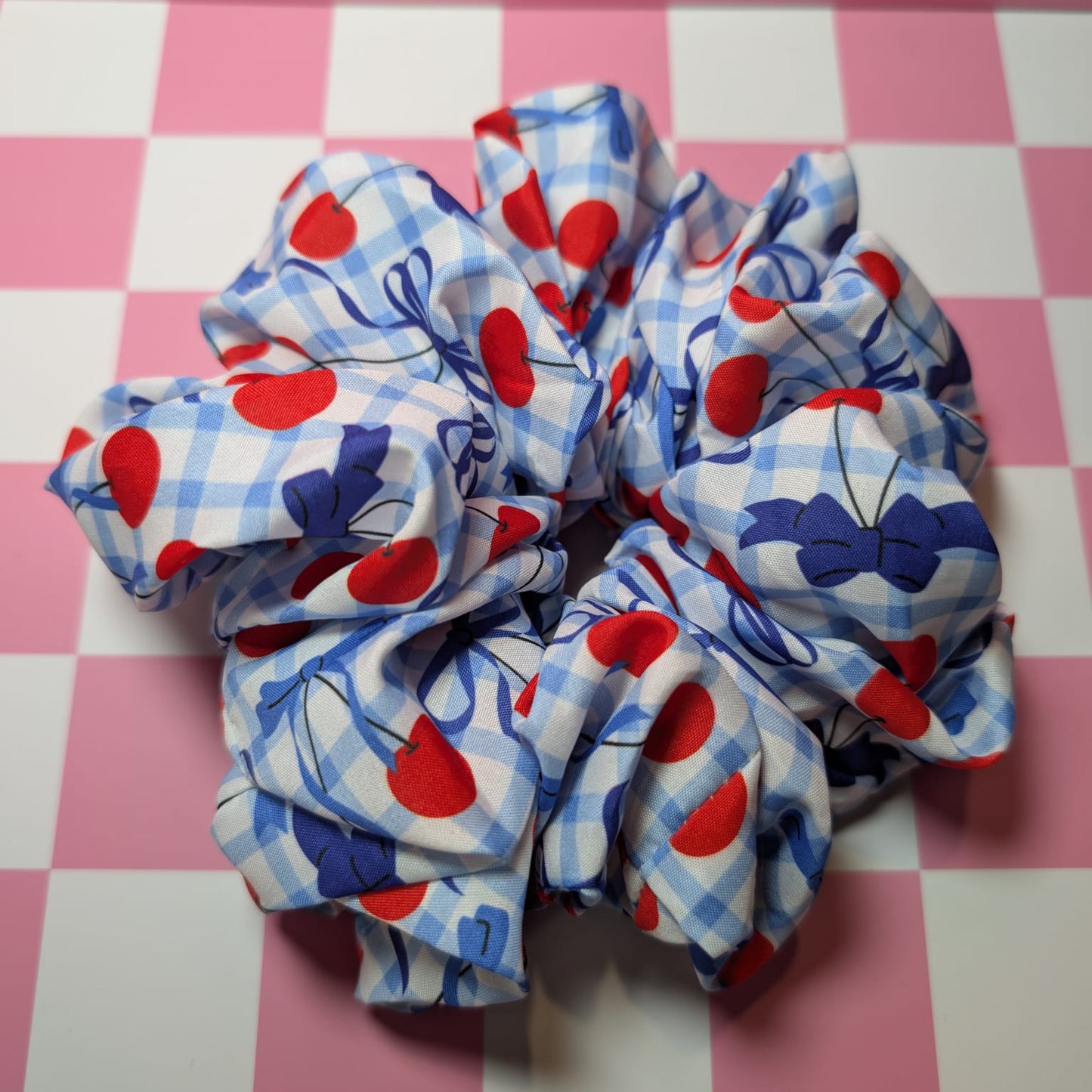 Two scrunchies with red, blue, and white pattern on a pink checkered background
