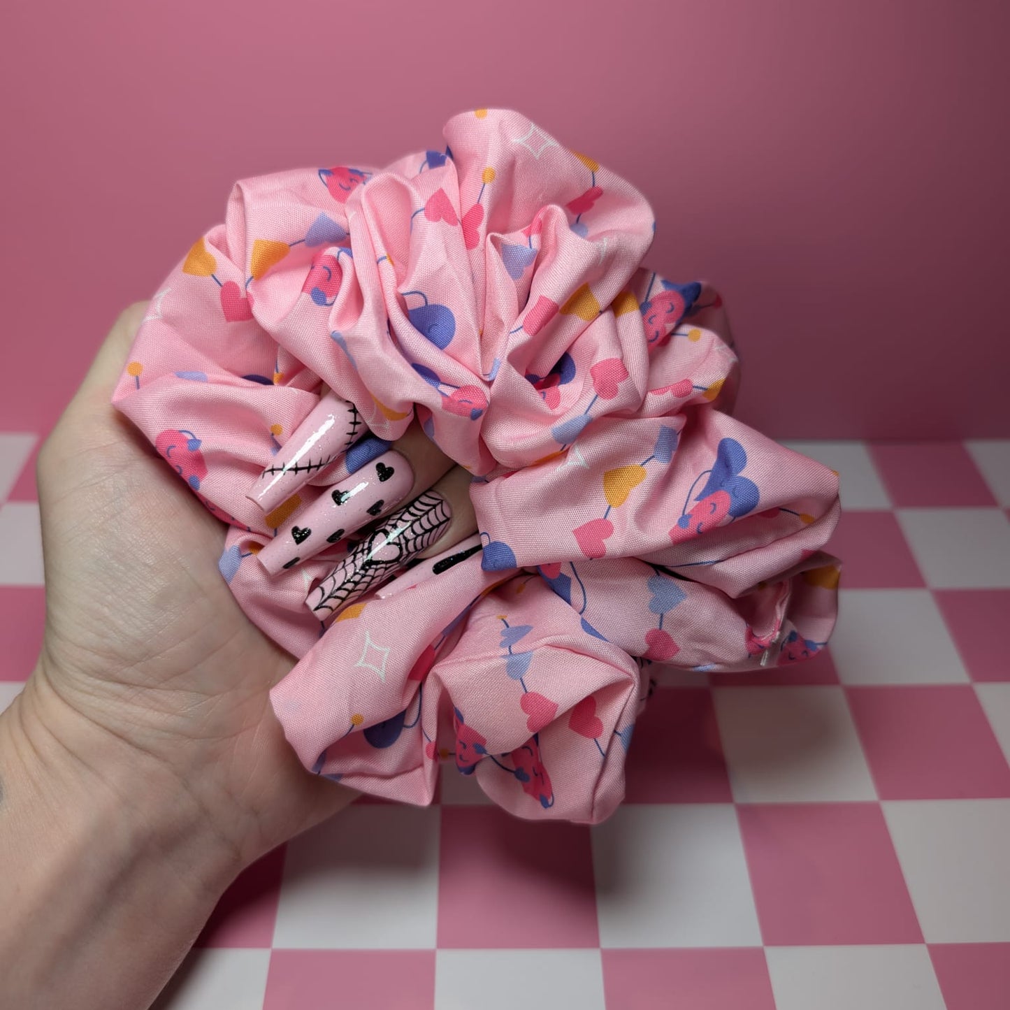 Pink scrunchie with colorful patterns held by a hand on a pink and white checkered surface.