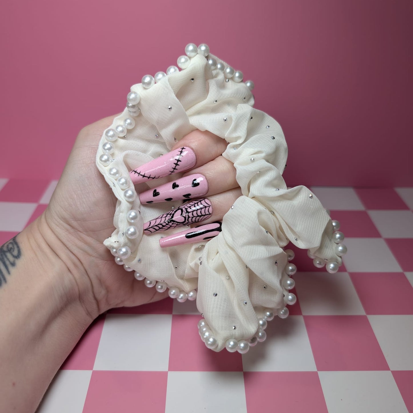 Hand holding a decorative hair scrunchie with pearls on a pink and white checkered background