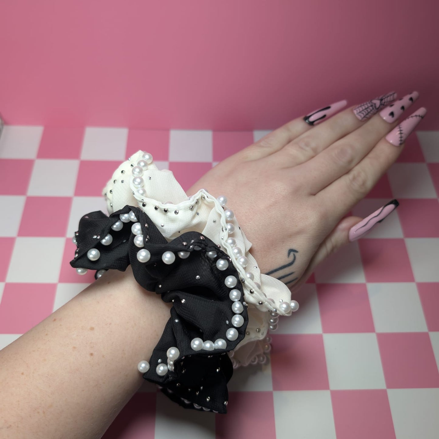 Hand wearing a black and white decorative bracelet on a pink and white checkered background