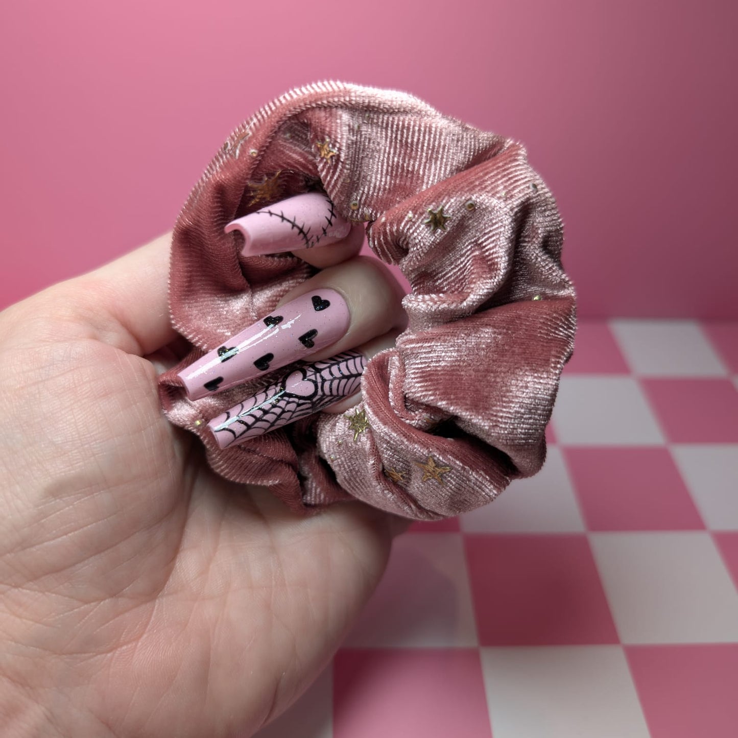 Pink scrunchie held by a hand against a pink and white checkered background