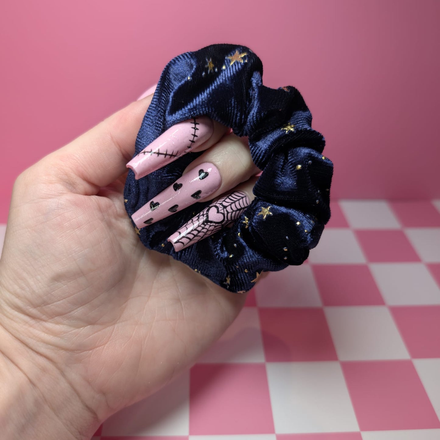 Navy blue scrunchie with decorative hair ties held in a hand against a pink checkered background