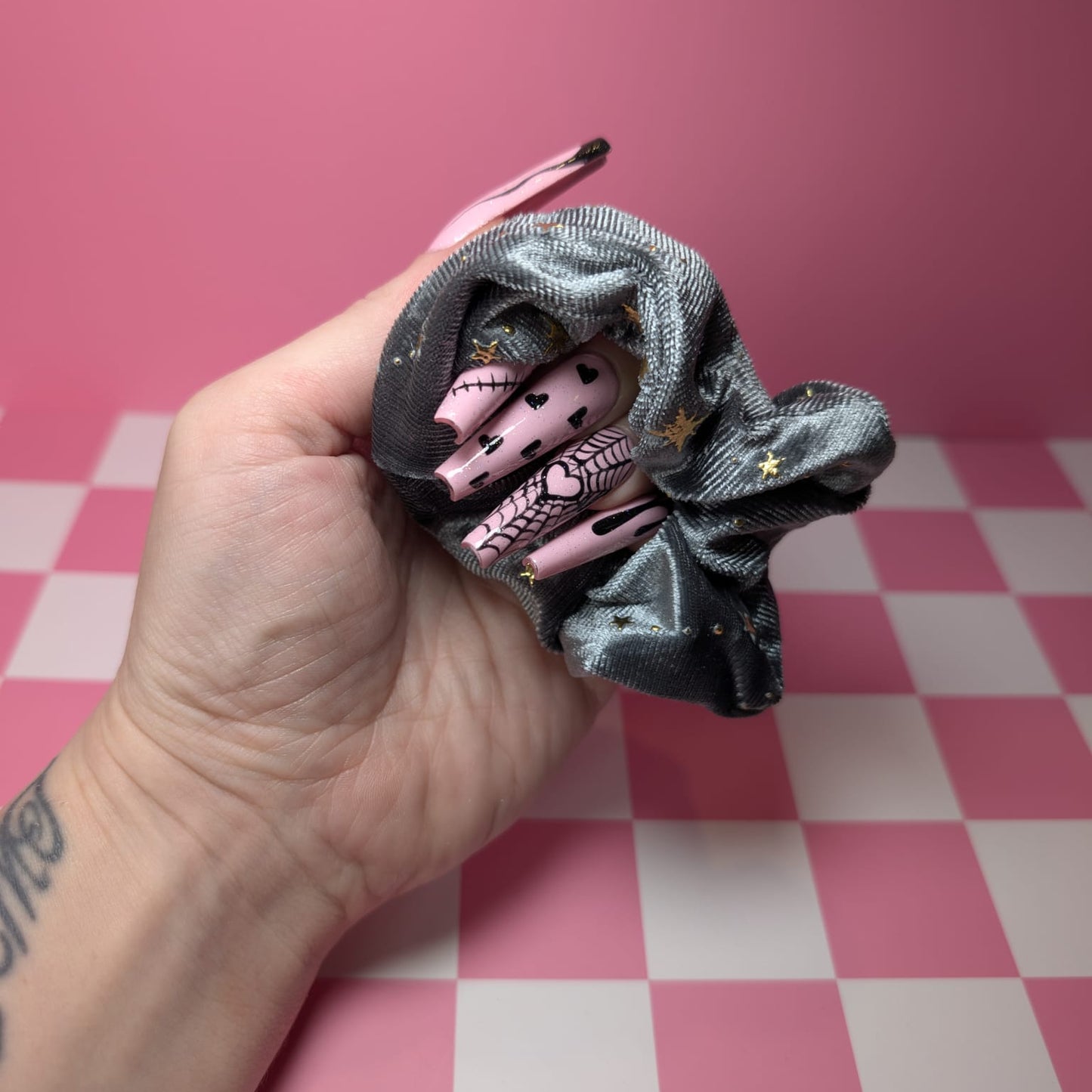 Black scrunchie held by a hand on a pink and white checkered background