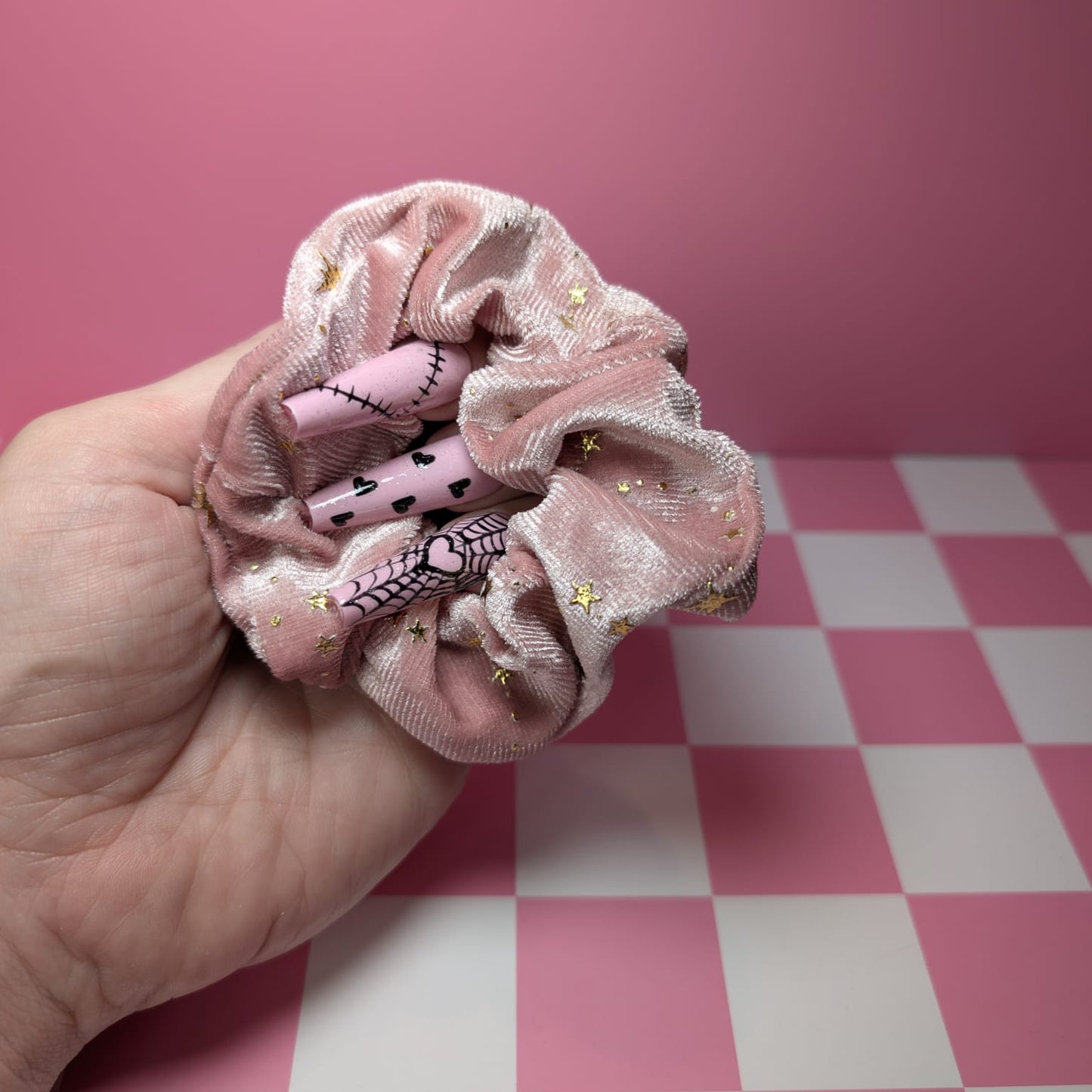 Pink scrunchie with cartoon character held by a hand on a pink and white checkered surface.