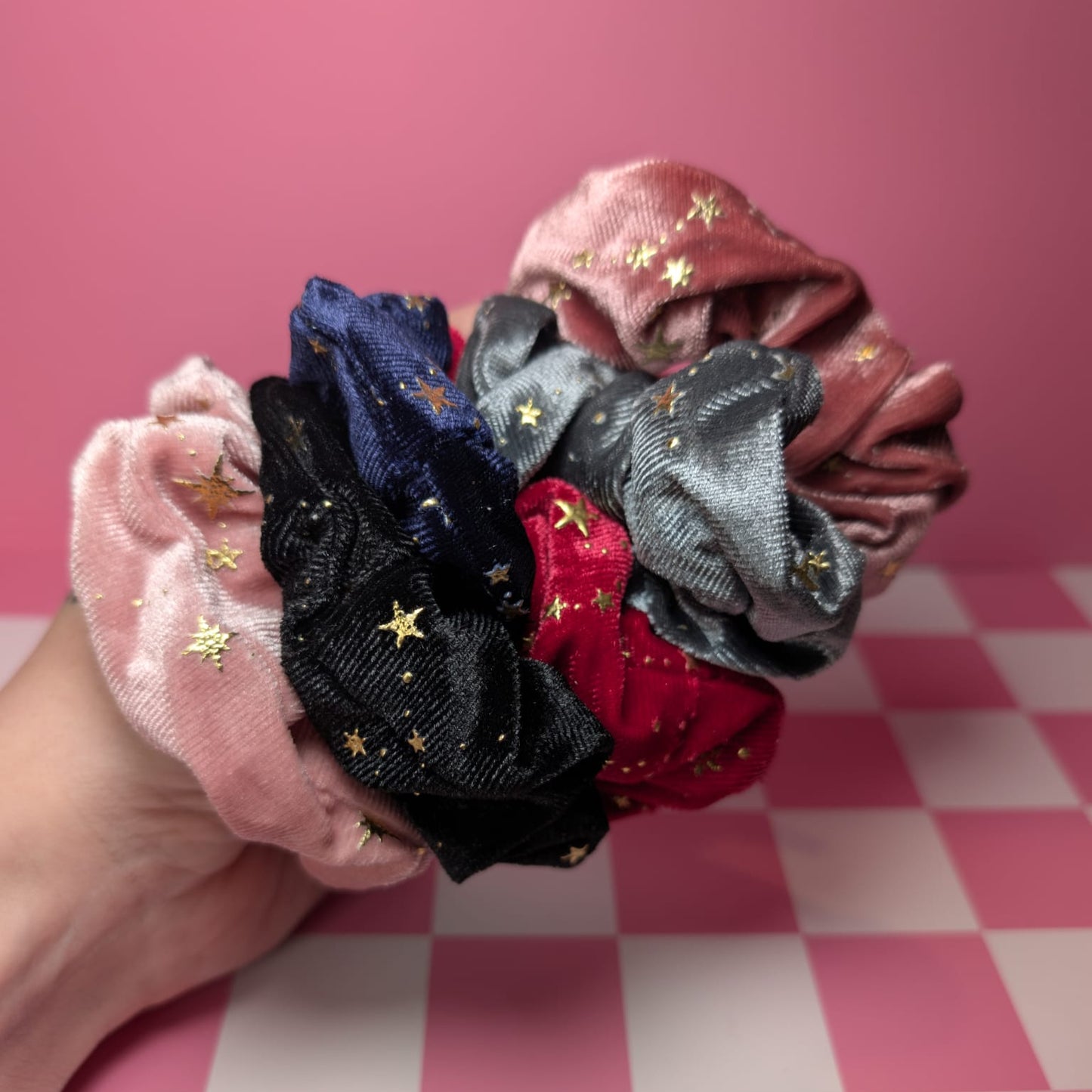 Collection of colorful scrunchies held by a hand on a pink checkered background