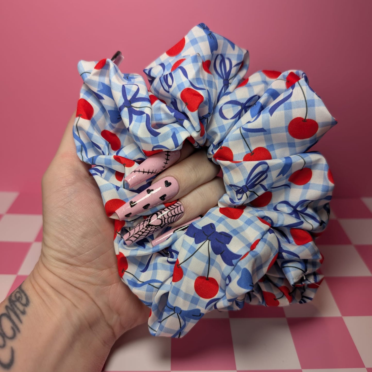 Three scrunchies with red hearts, blue plaid patterns, and cartoon characters on a pink checkered background.