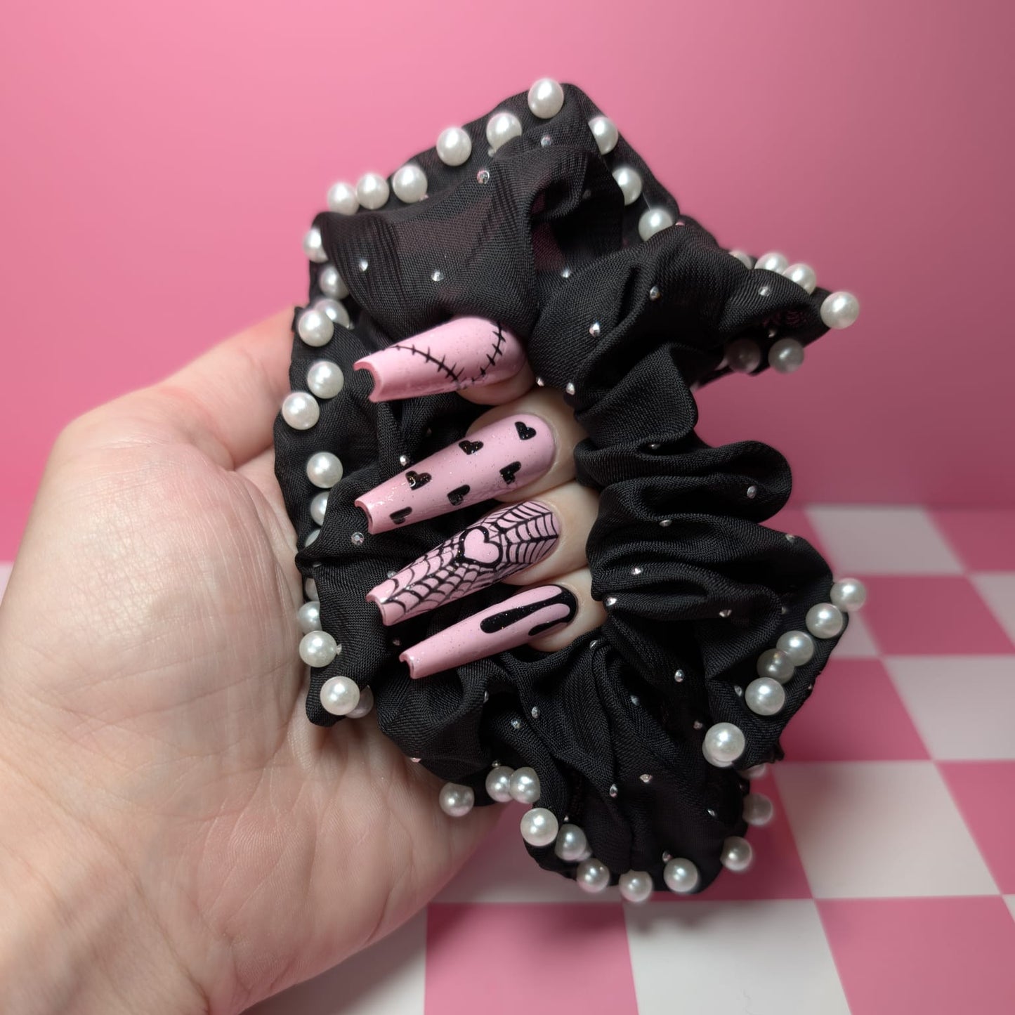 Black scrunchie with pink and black hair clips held by a hand on a pink and white checkered background
