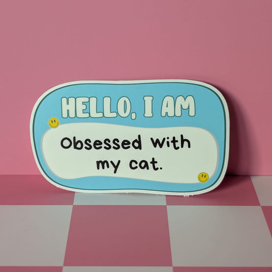 Sticker with text 'HELLO, I AM Obsessed with my cat.' on a pink and white checkered background