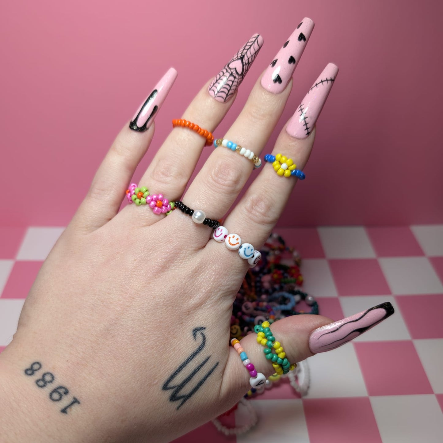 Hand with colorful nail art and bracelets on a pink checkered background