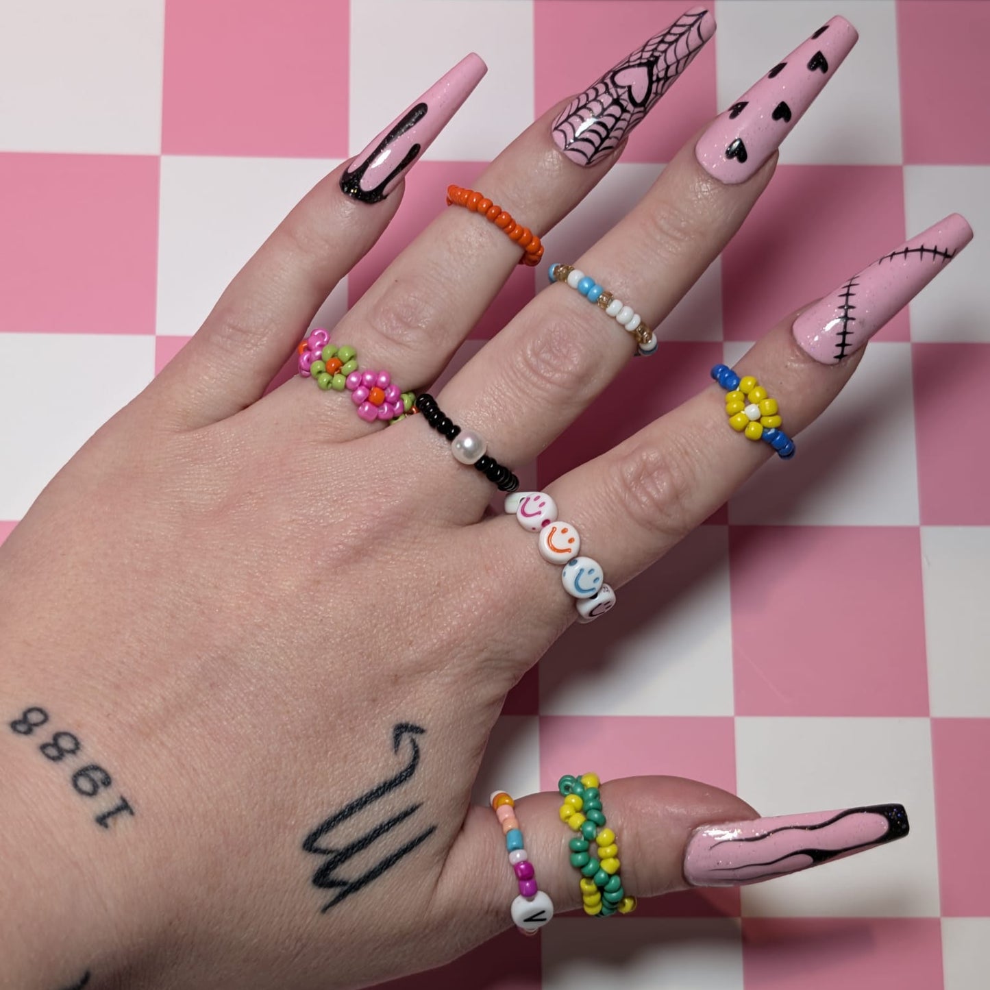 Hand with colorful nail art and rings on a pink and white checkered background