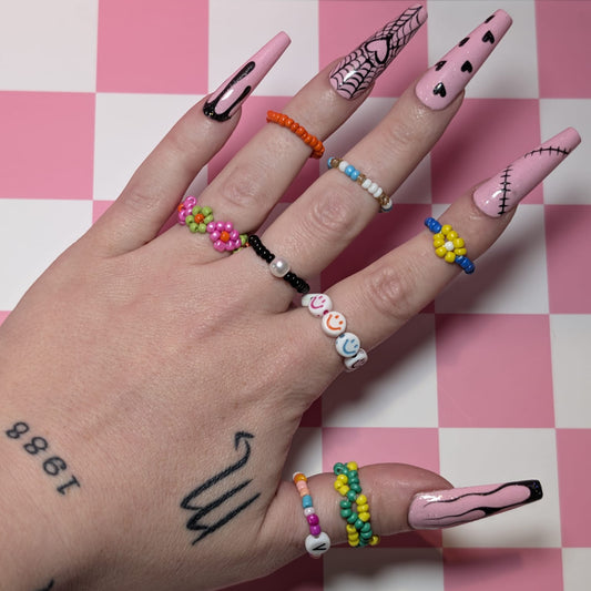 Hand with colorful nail art and rings on a pink and white checkered background