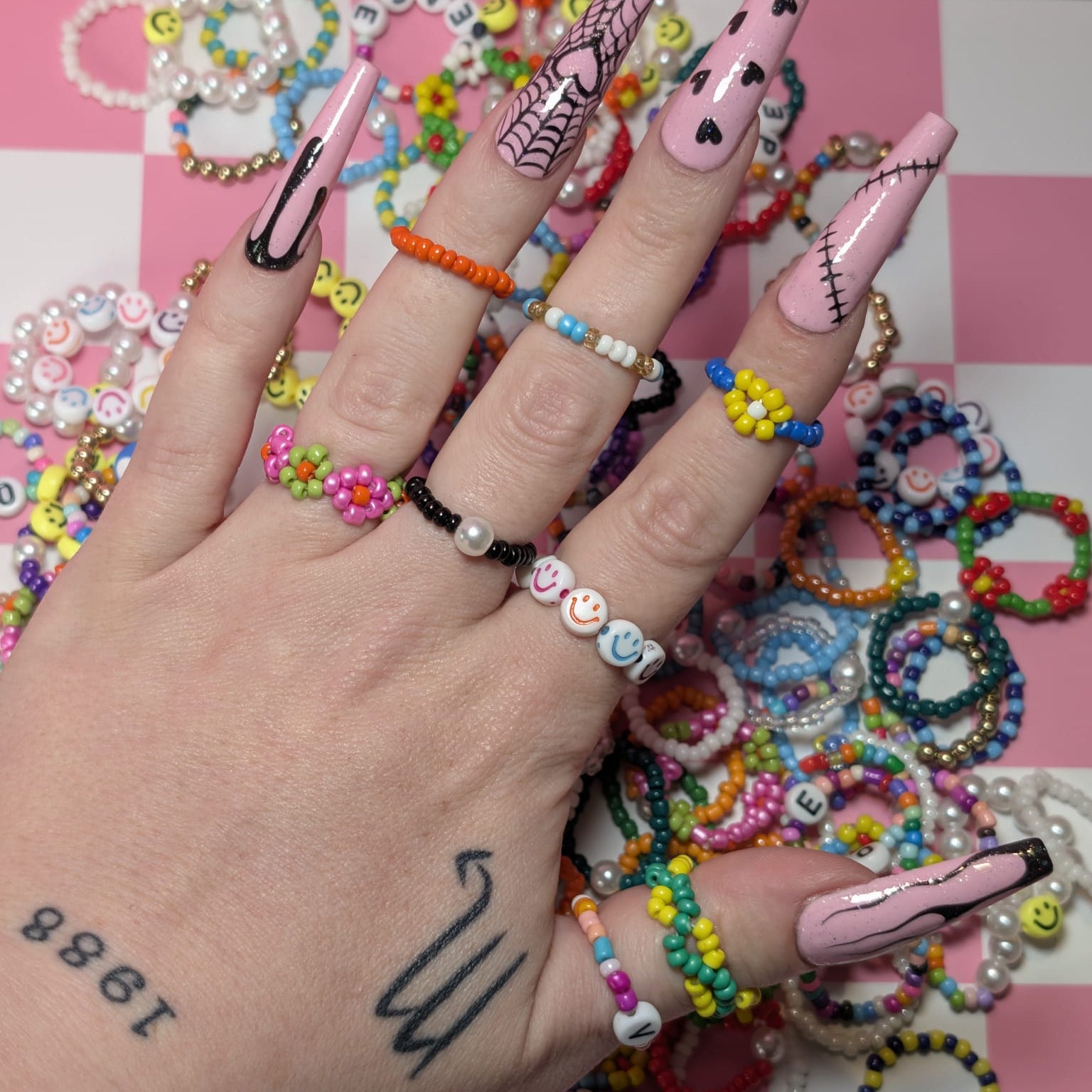 Hand with colorful nail art and bracelets on a pink checkered background