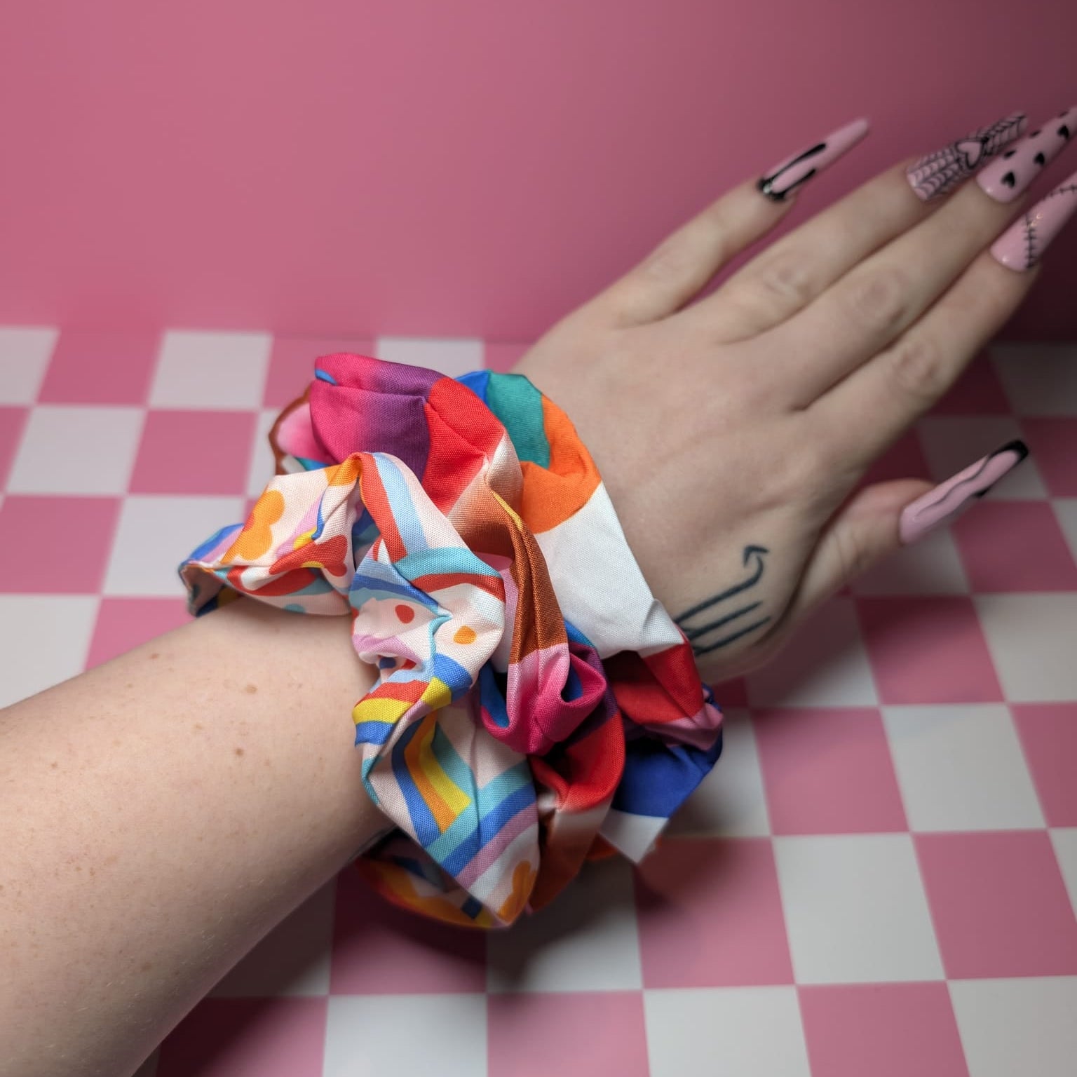Colorful scrunchies on a wrist with a pink checkered background