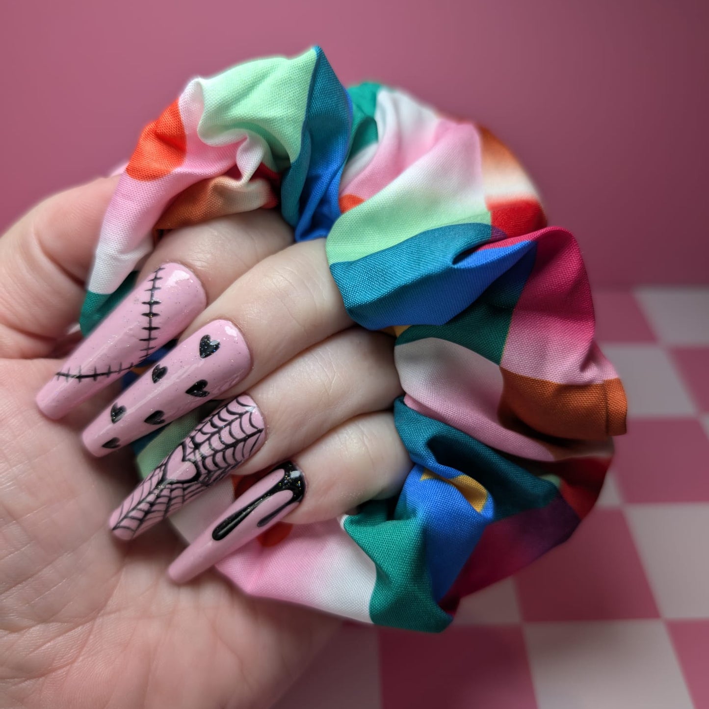 Hand holding a colorful scrunchie with checkered pink and white background