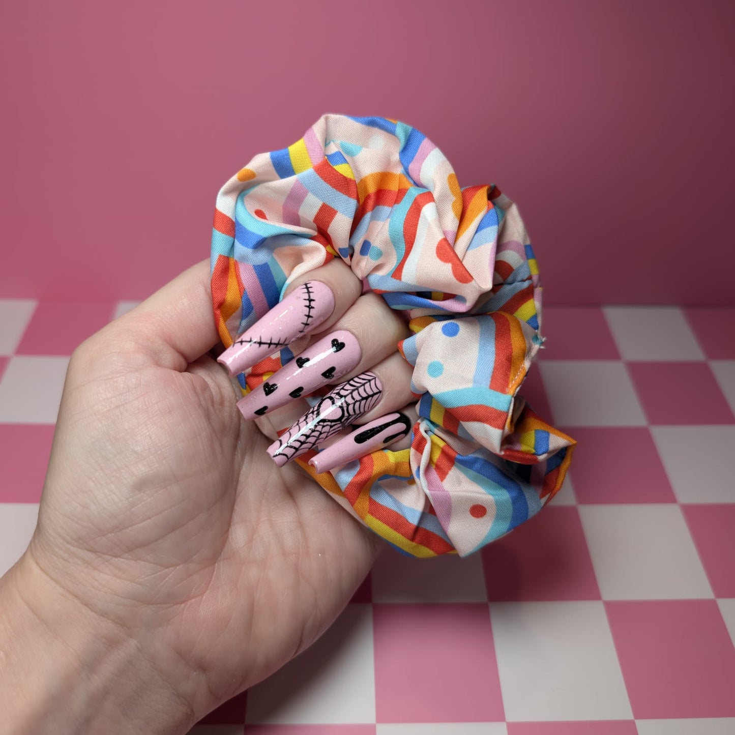 Colorful scrunchie held by a hand on a pink and white checkered background