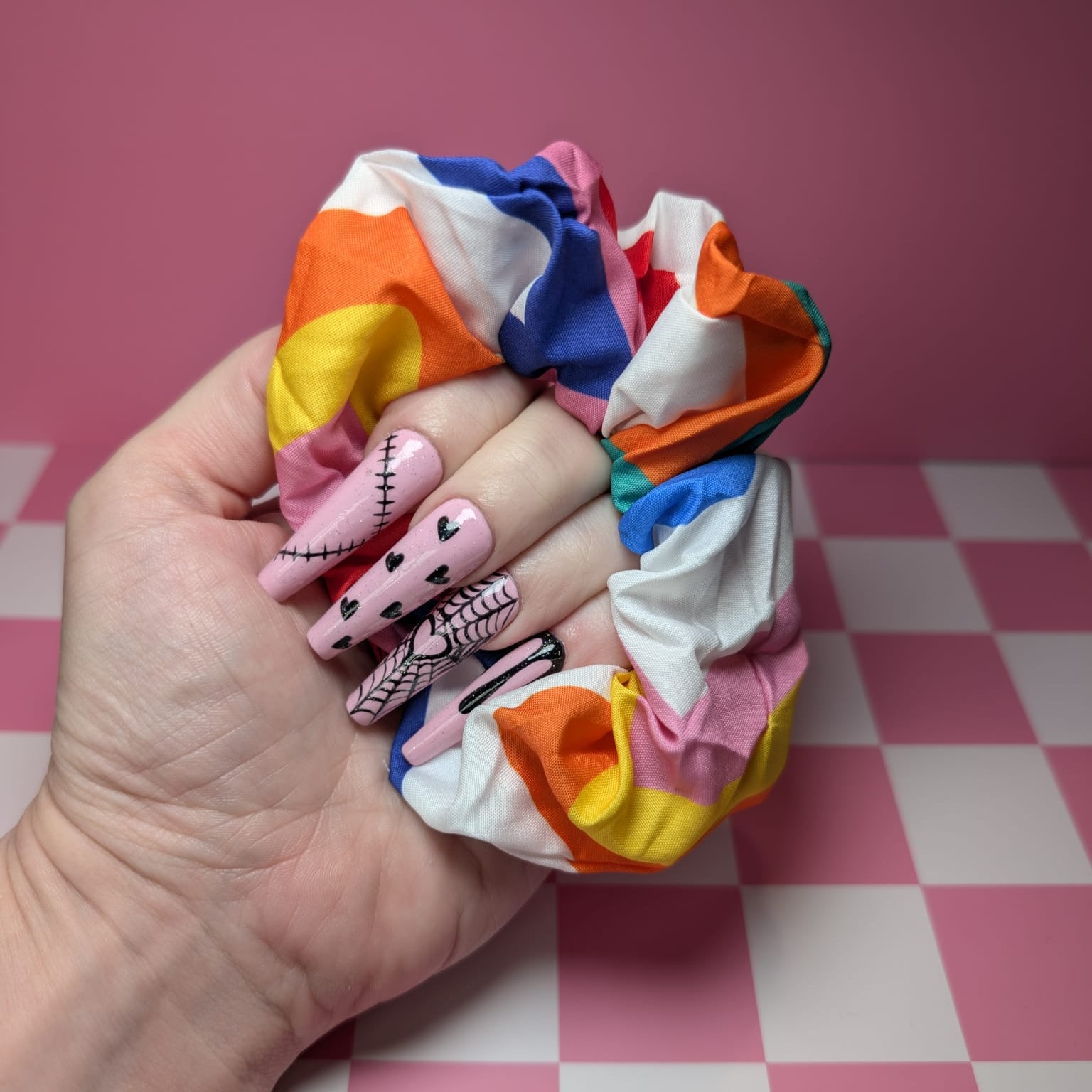 Hand holding colorful scrunchies with a pink and white checkered background