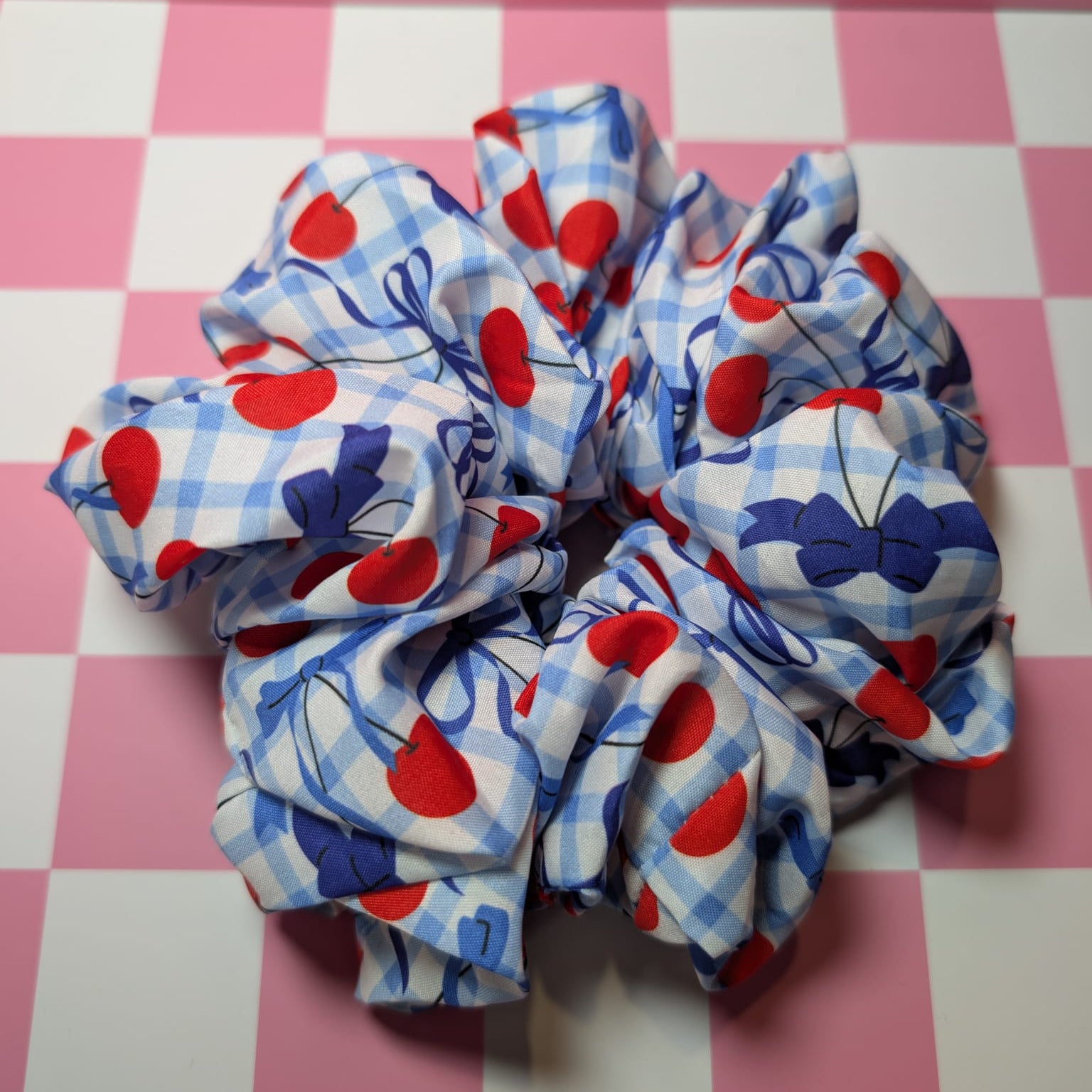Two scrunchies with red, blue, and white pattern on a pink checkered background