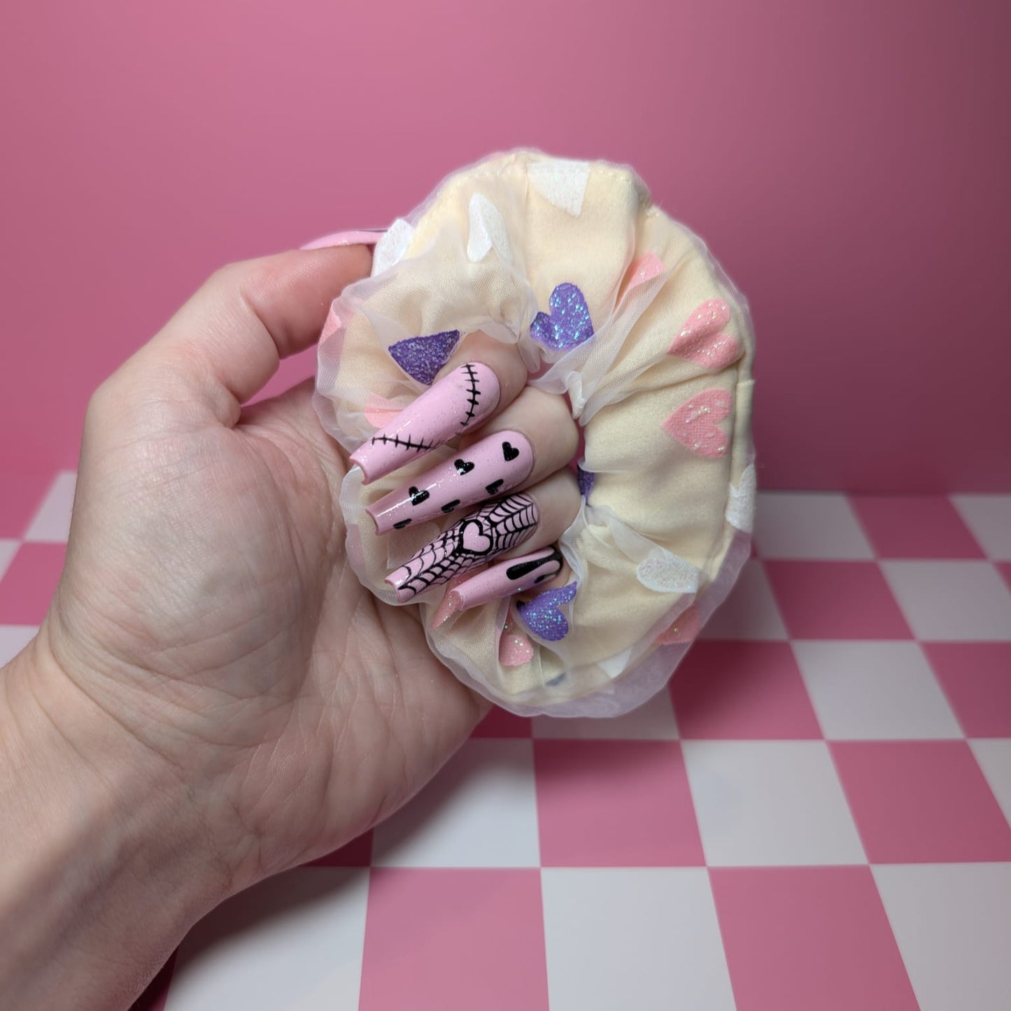 Hand holding a small plush toy with a checkered pink and white background