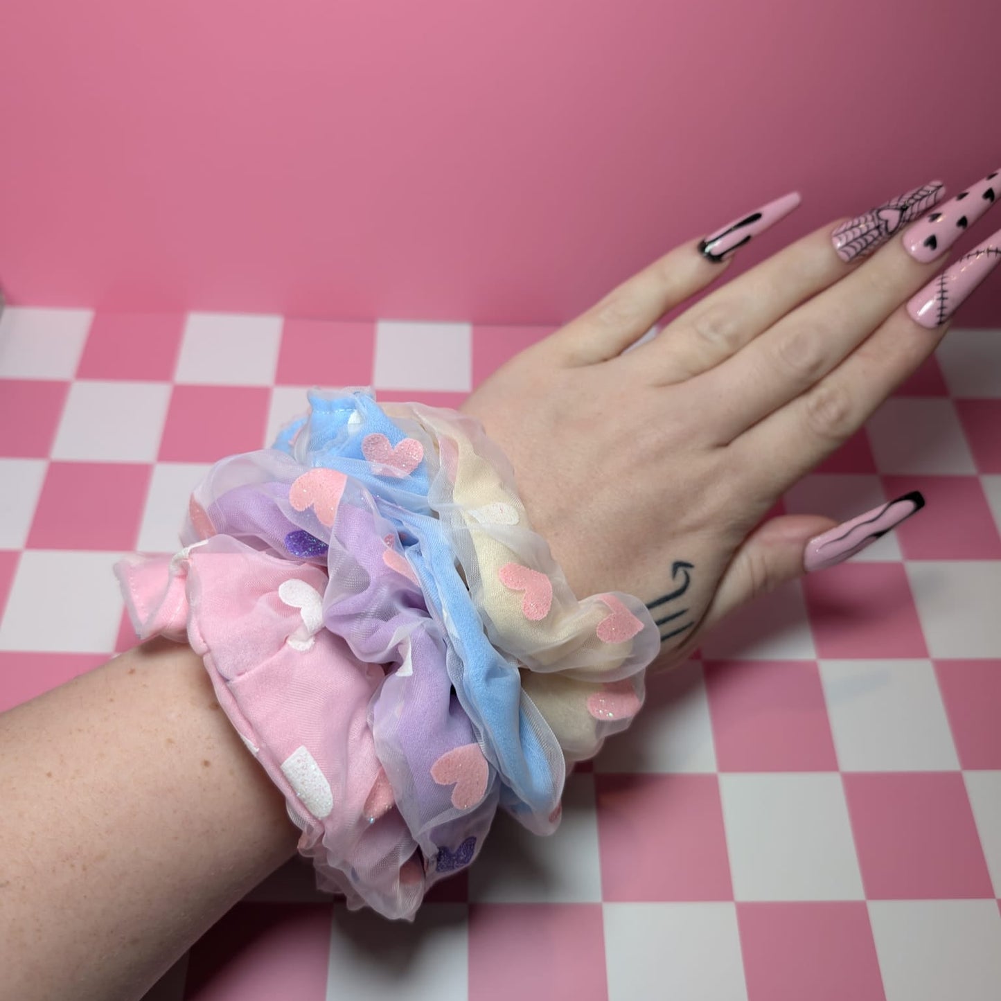 Hand with colorful scrunchies on a pink and white checkered background