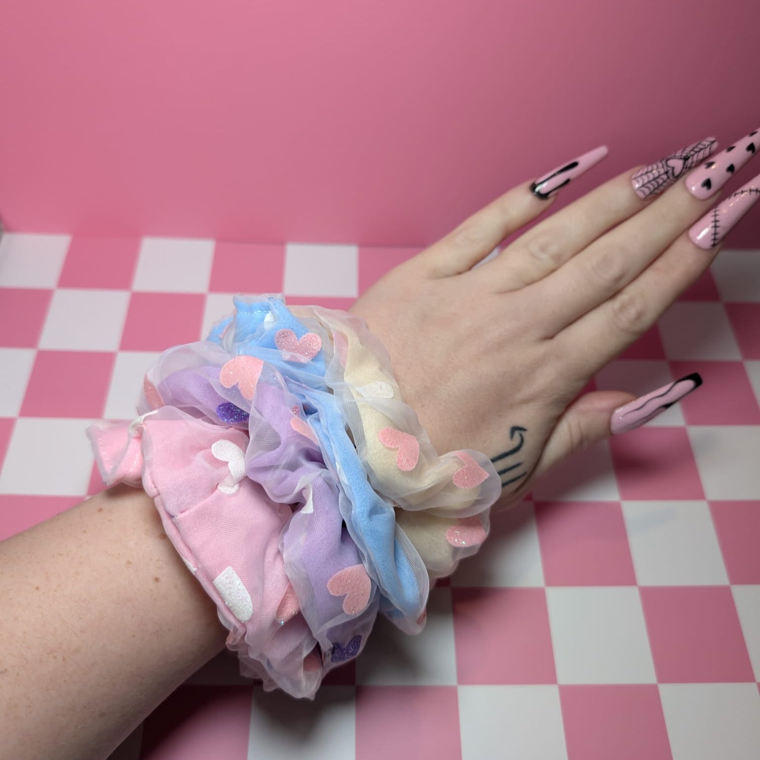 Hand with colorful scrunchies on a pink and white checkered background