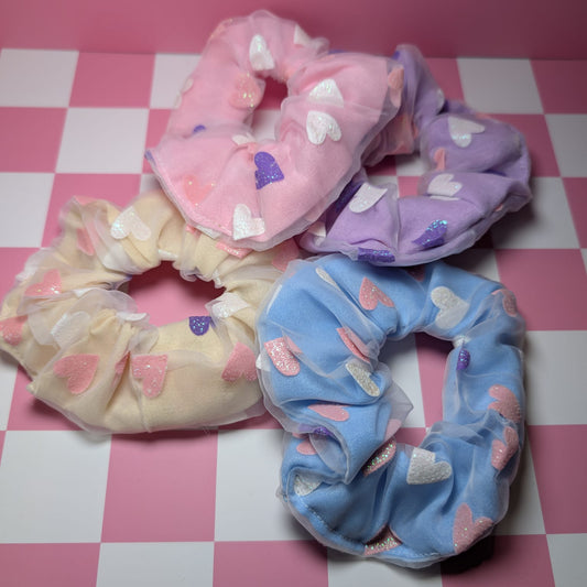 Four colorful scrunchies with heart patterns on a pink checkered background