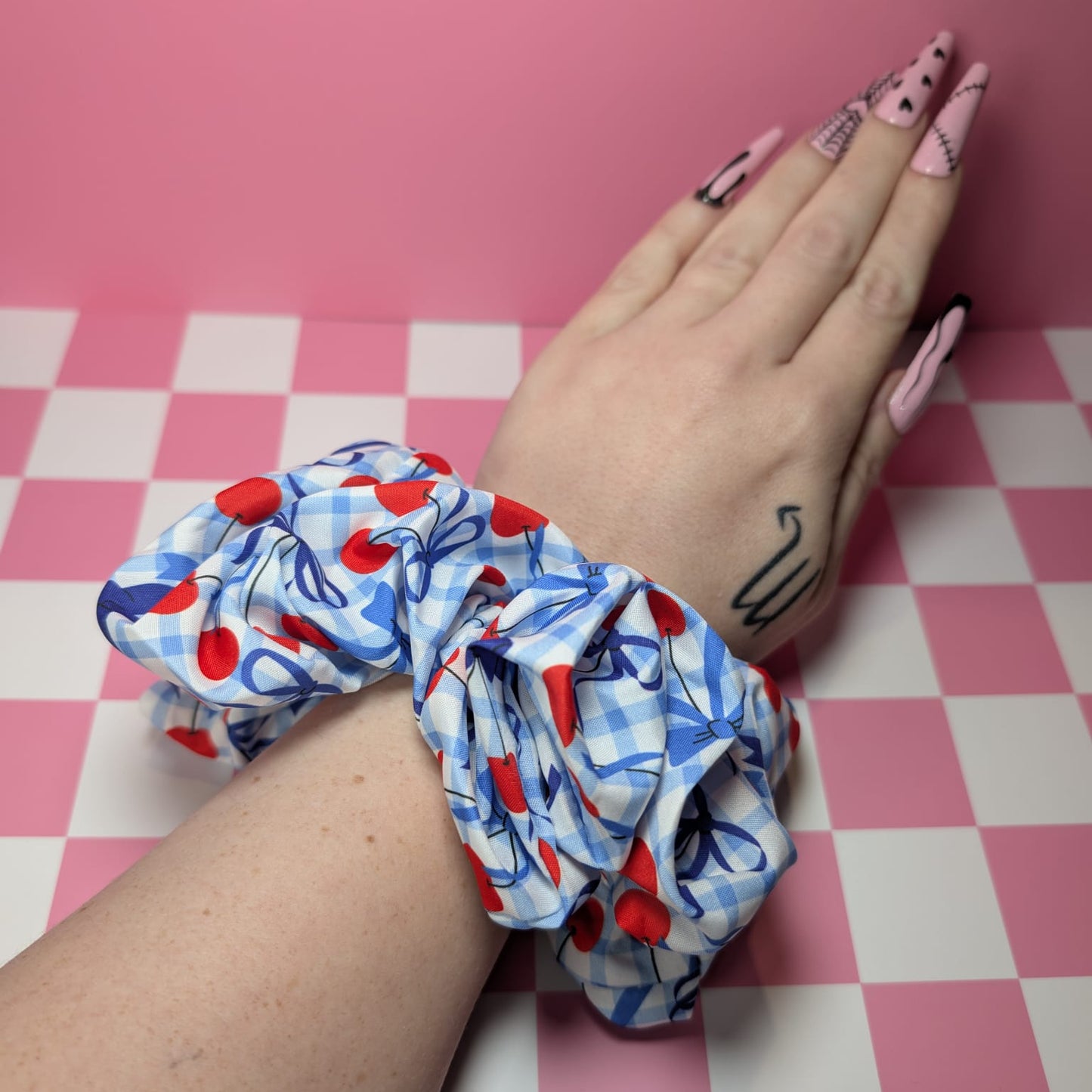 Hand wearing a colorful scrunchie on a pink and white checkered background