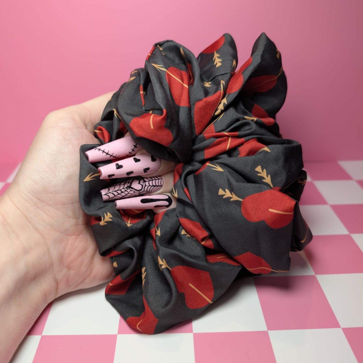 Hand holding a black scrunchie with red floral patterns on a pink and white checkered background