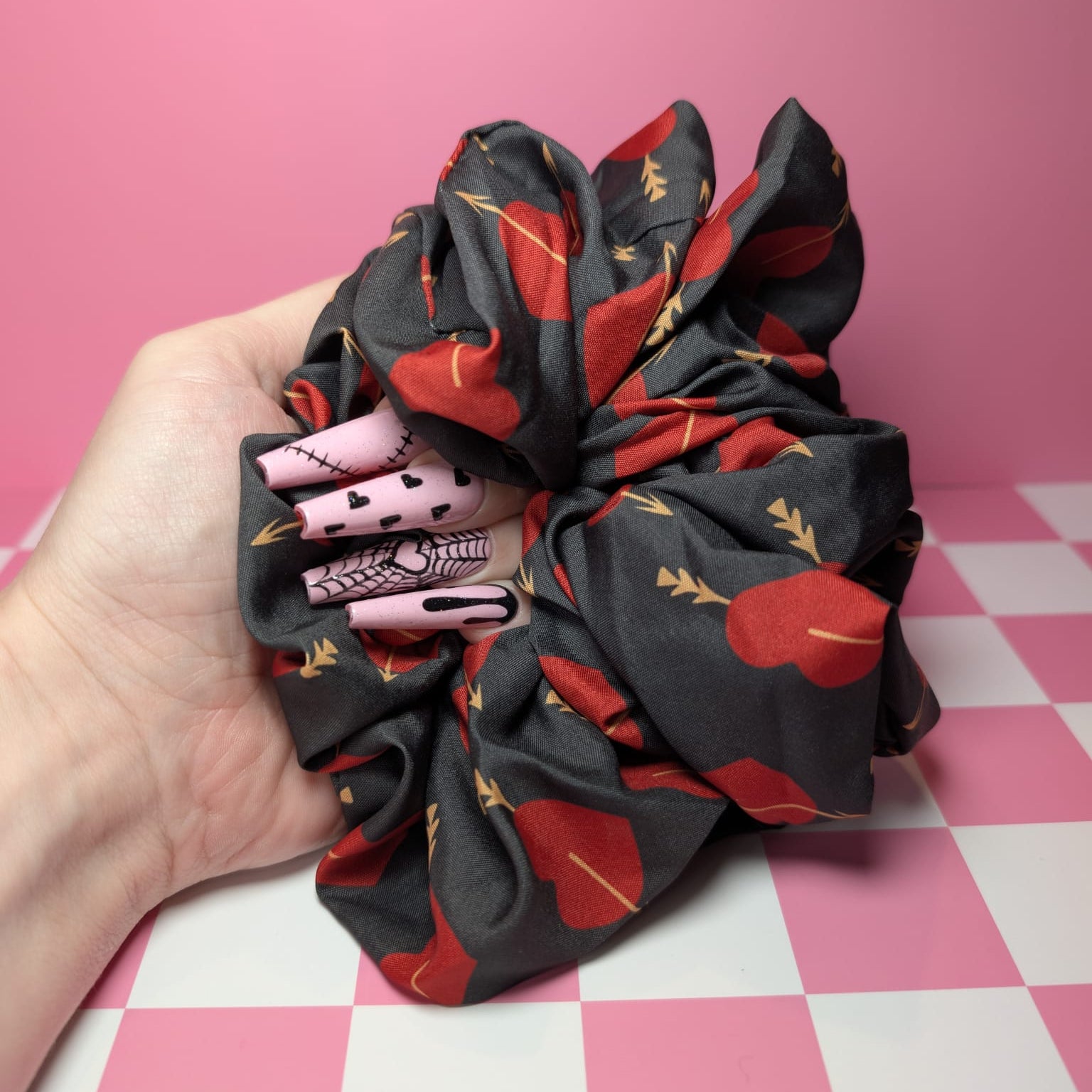 Hand holding a black scrunchie with red floral patterns on a pink and white checkered background