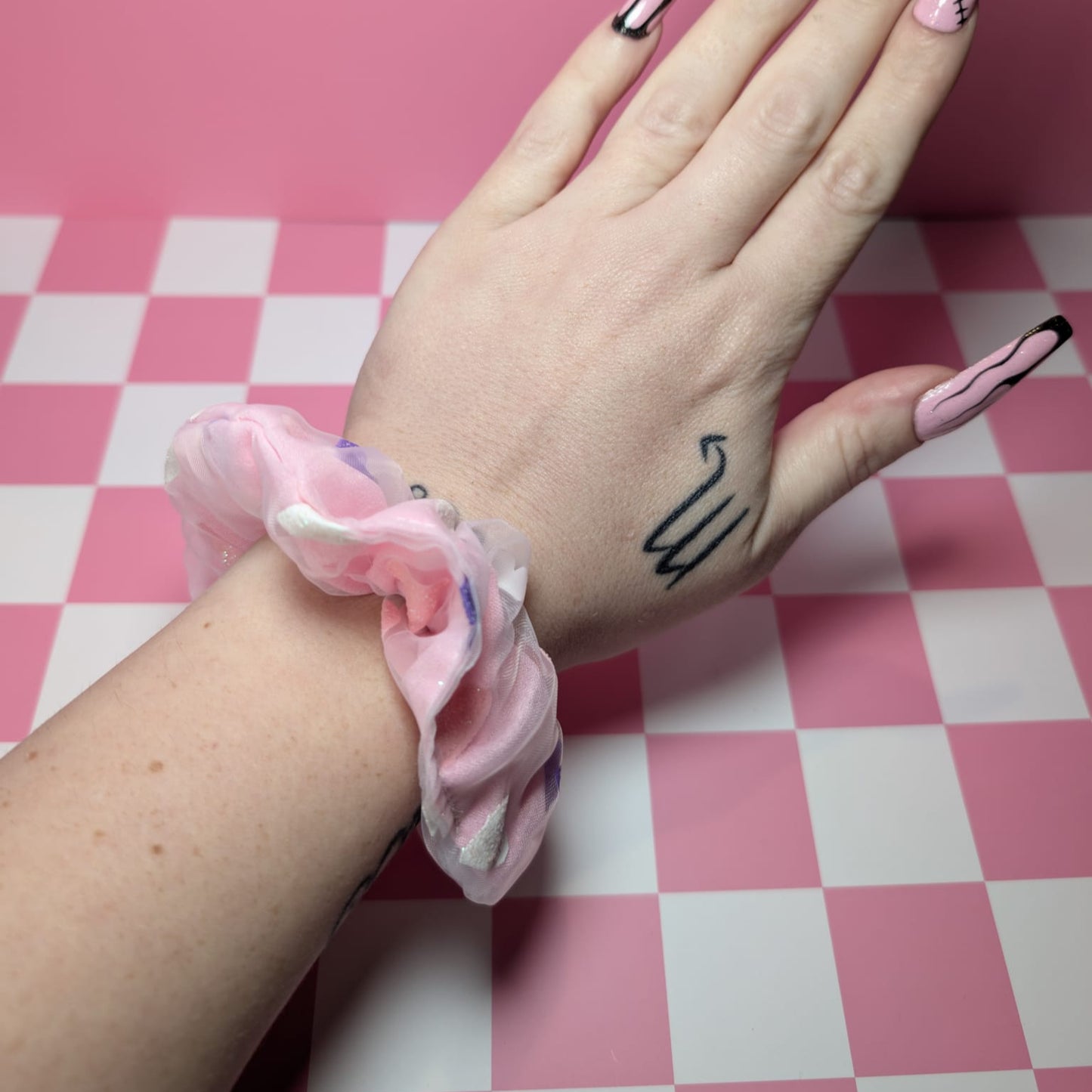 Hand with pink nail polish and a scrunchie on a pink and white checkered background