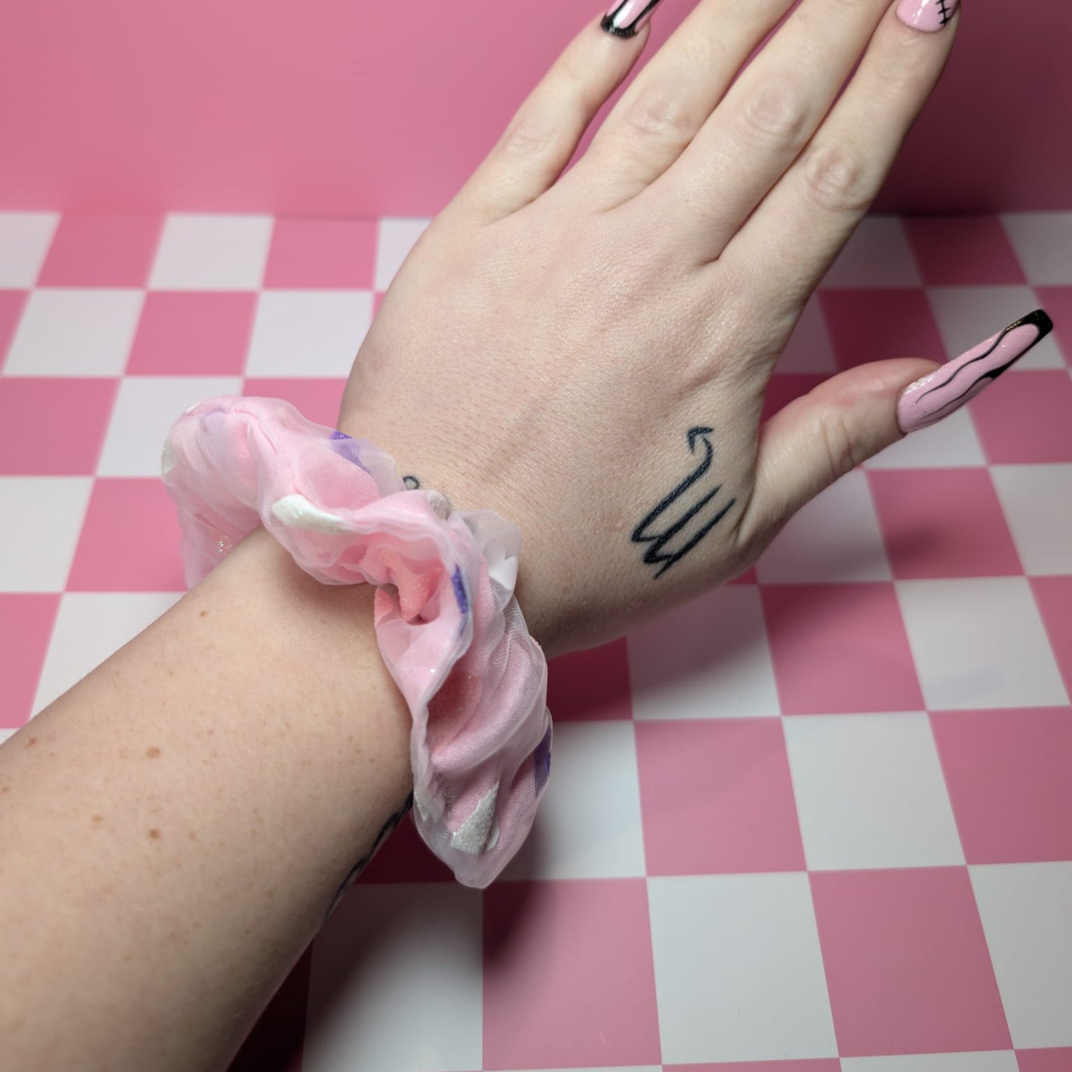 Hand with pink nail polish and a scrunchie on a pink and white checkered background