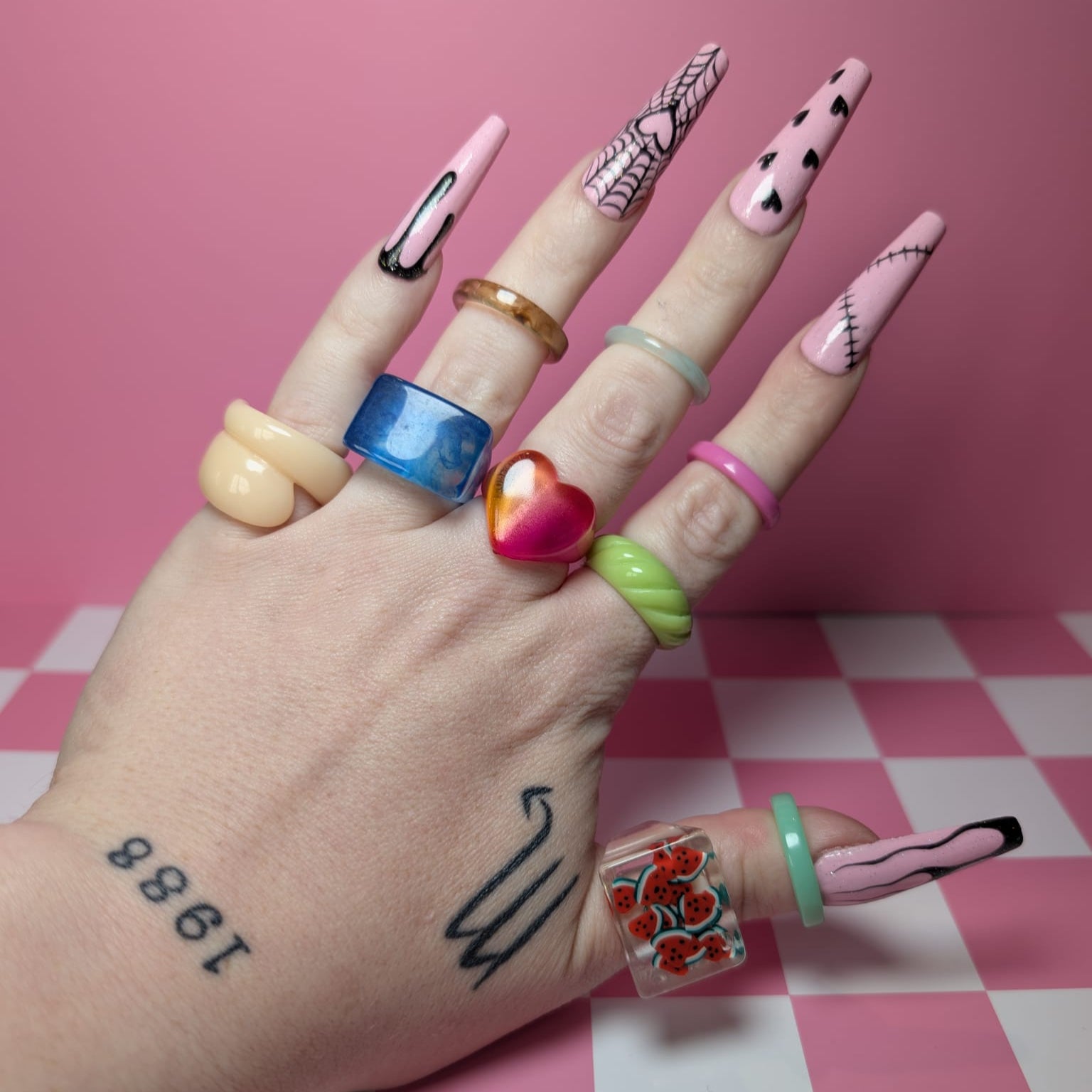 Hand with colorful nail art and rings on a pink checkered background