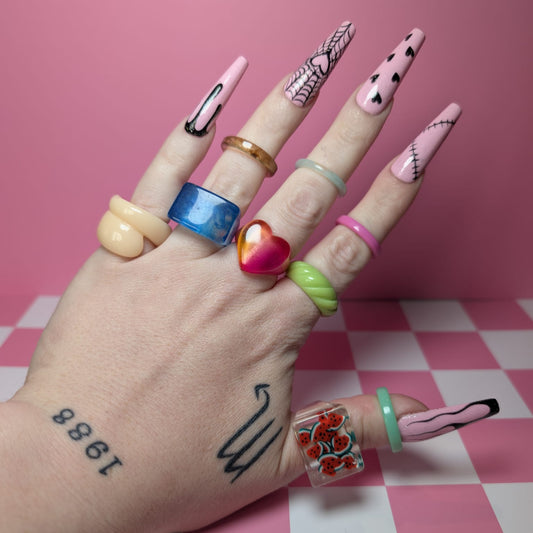 Hand with colorful nail art and rings on a pink checkered background