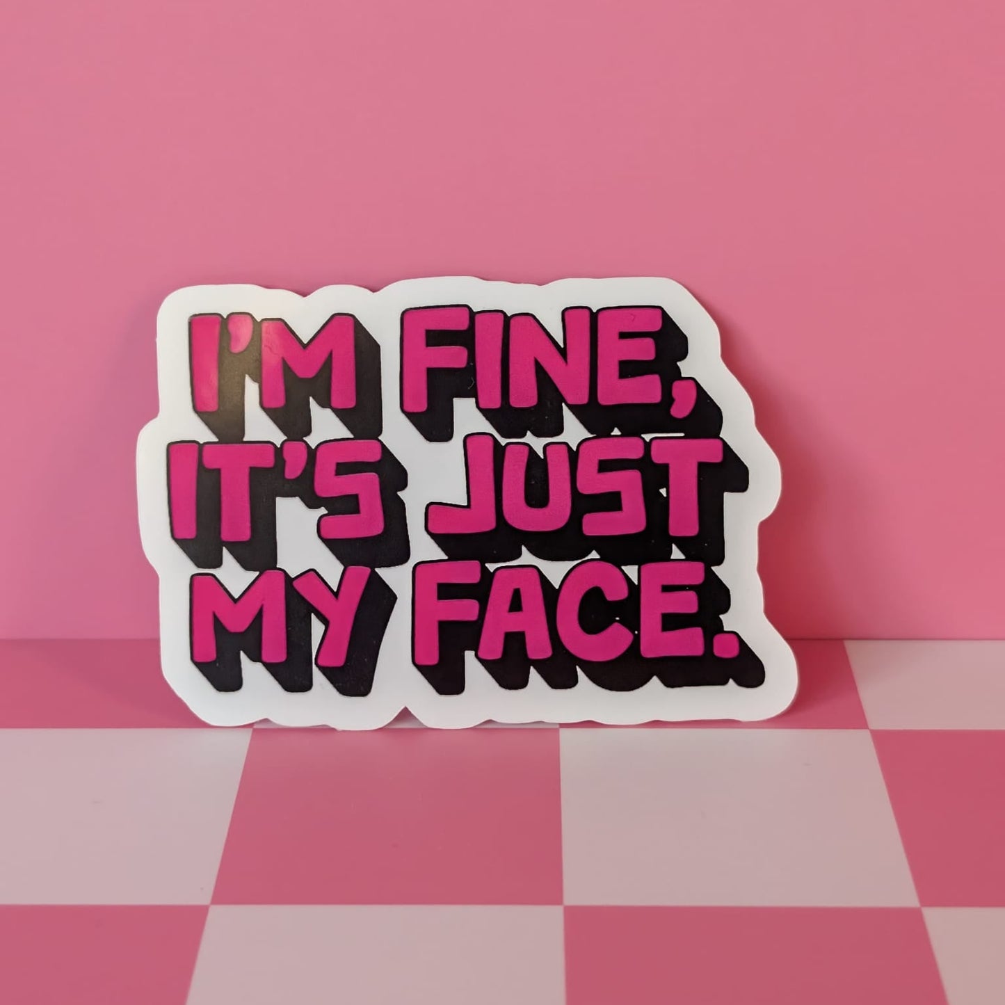 Sticker with 'I'm fine, it's just my face' text on a pink checkered surface