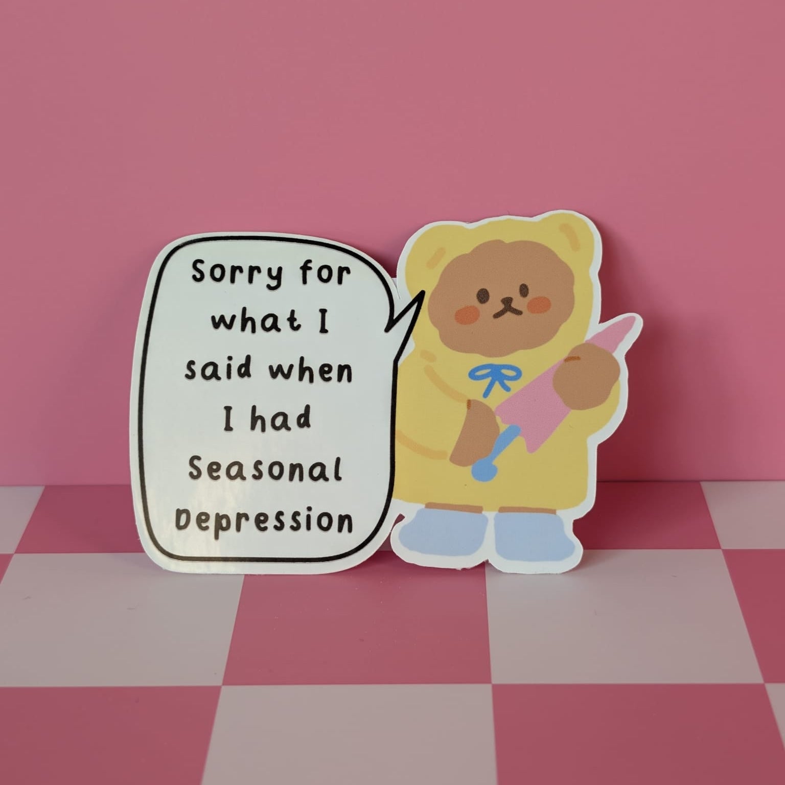 Sticker of a bear holding a pink ribbon with text on a pink and white checkered background
