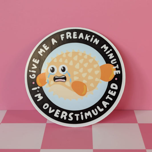 Sticker with cartoon character and text 'Give me a freakin minute, I'm overstimulated' on a pink background