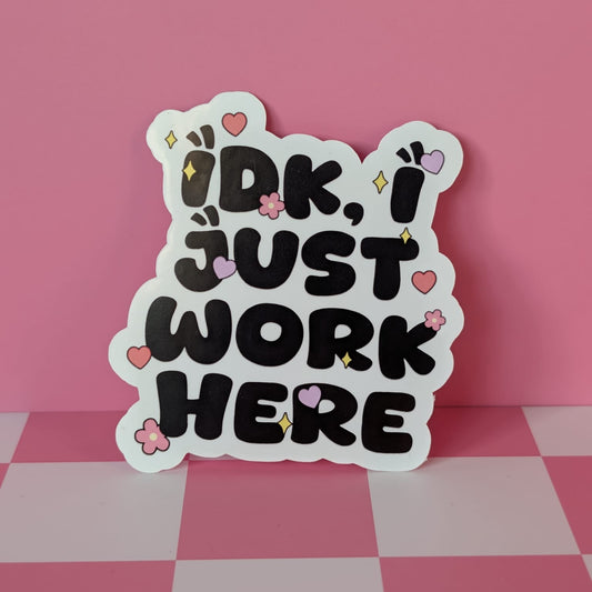 Decorative sign with 'IDK, I just work here' text on a pink and white checkered surface.
