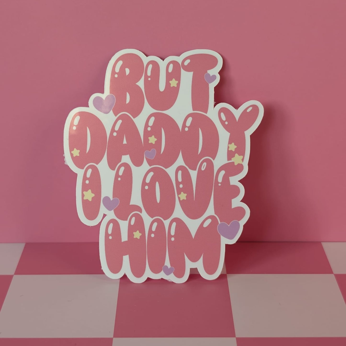 Decorative sign with 'But Daddy Love Him' text on a pink checkered floor.