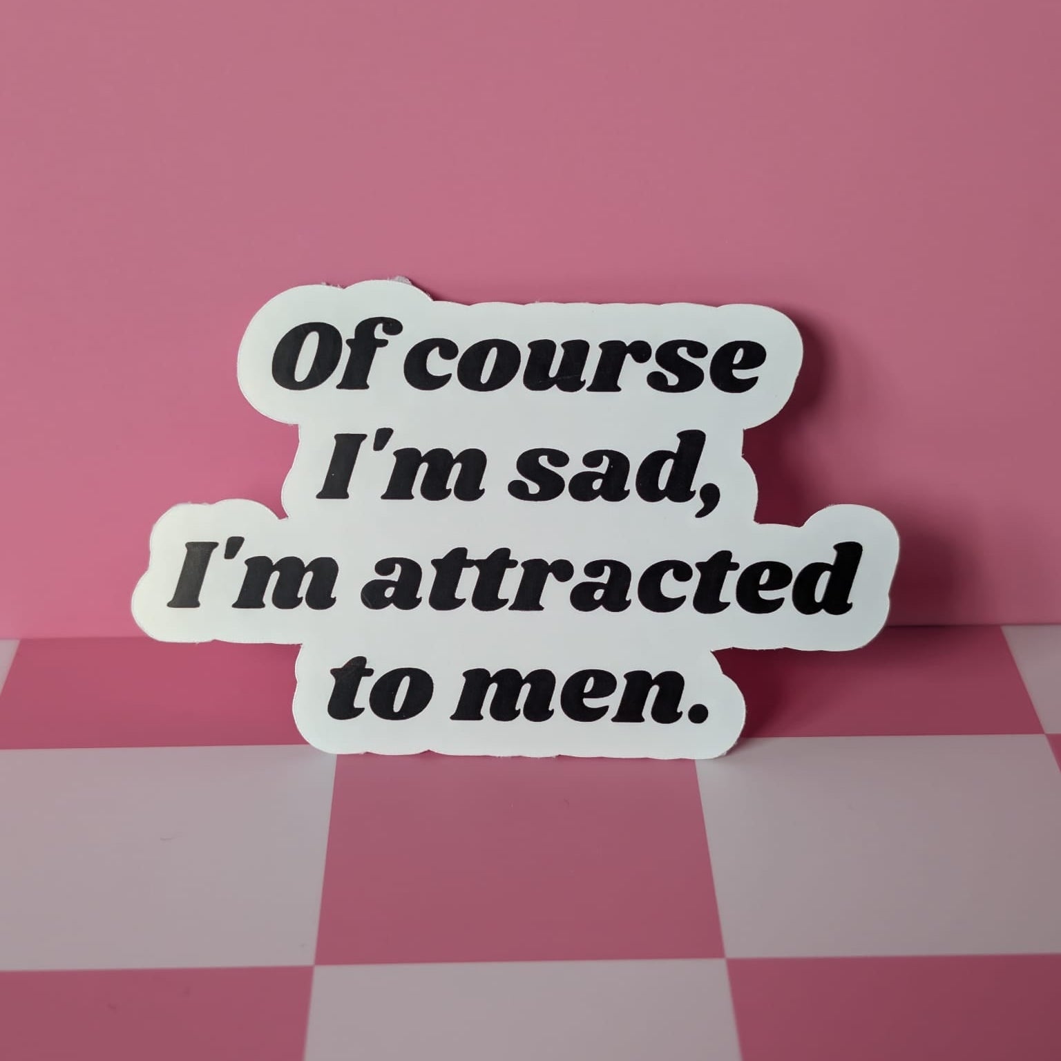 Sticker with text 'Of course I'm sad, I'm attracted to men' on a pink checkered background