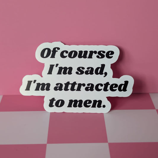 Sticker with text 'Of course I'm sad, I'm attracted to men' on a pink checkered background