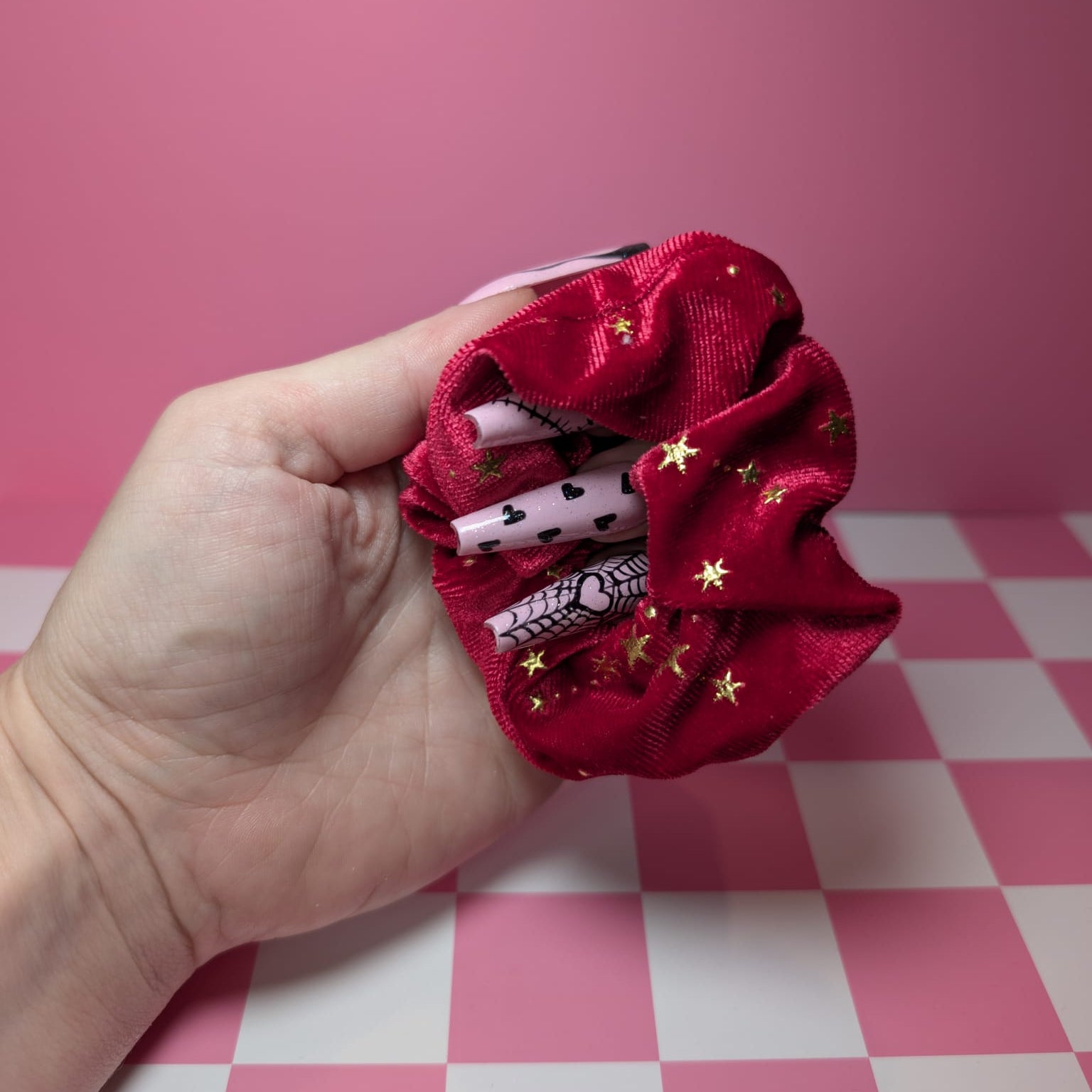 Red scrunchie with decorative elements held by a hand against a pink and white checkered background